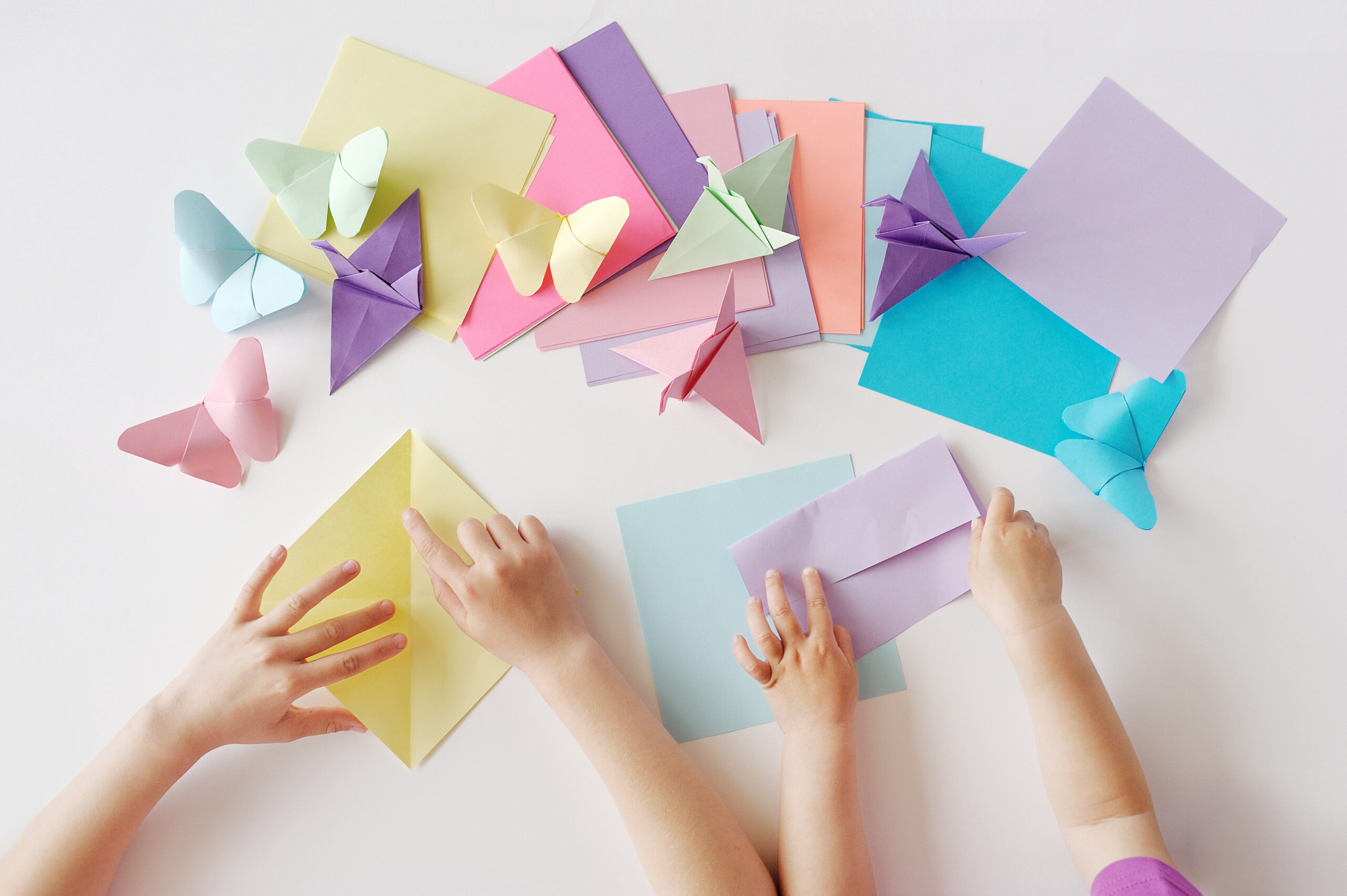 Children's hands do origami from colored paper on white background. lesson of origami